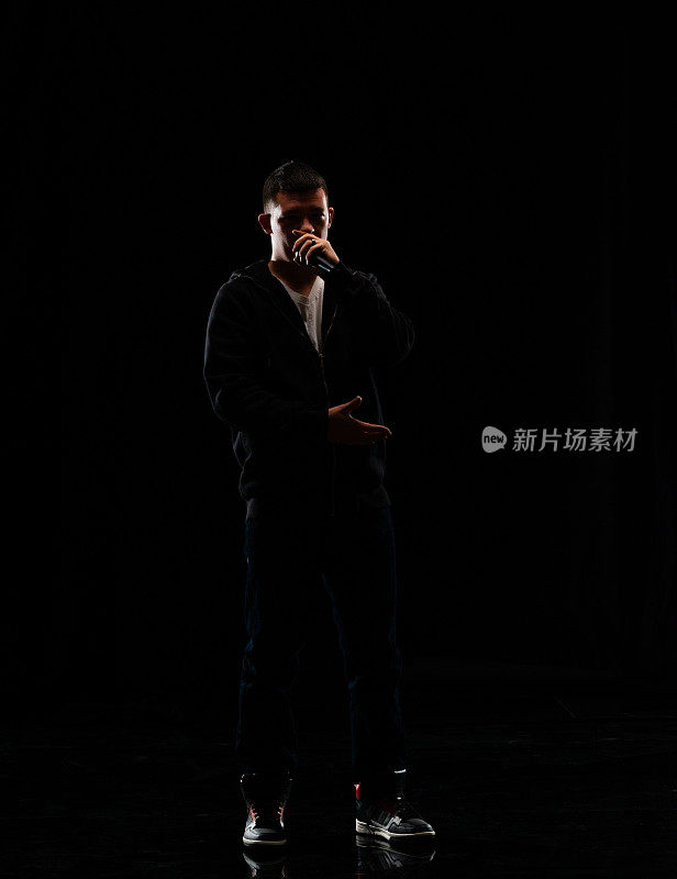 全长/一人/一人/正面的观点20-29岁的成年英俊的人高加索男性/年轻男子歌手/音乐家站/跳舞在黑人背景谁是唱歌/高兴和拿着麦克风